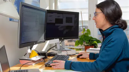 En kvinna med mörkt hår sitter framför datorn och programmerar.