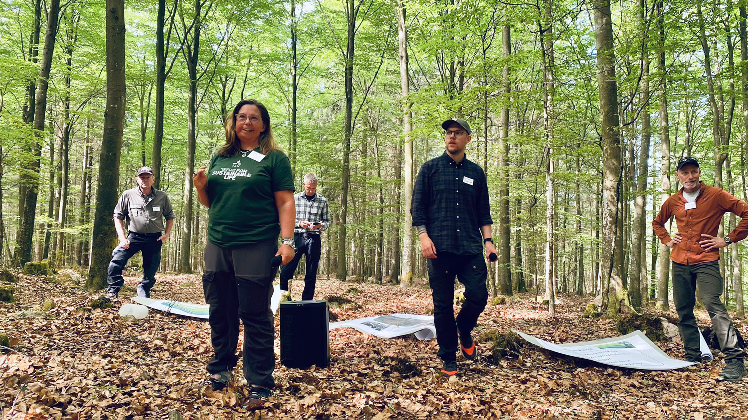 En leende kvinna i grön tshirt står tillsammans med några andra personer i en lövskog. 