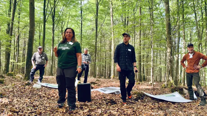 En leende kvinna i grön tshirt står tillsammans med några andra personer i en lövskog.