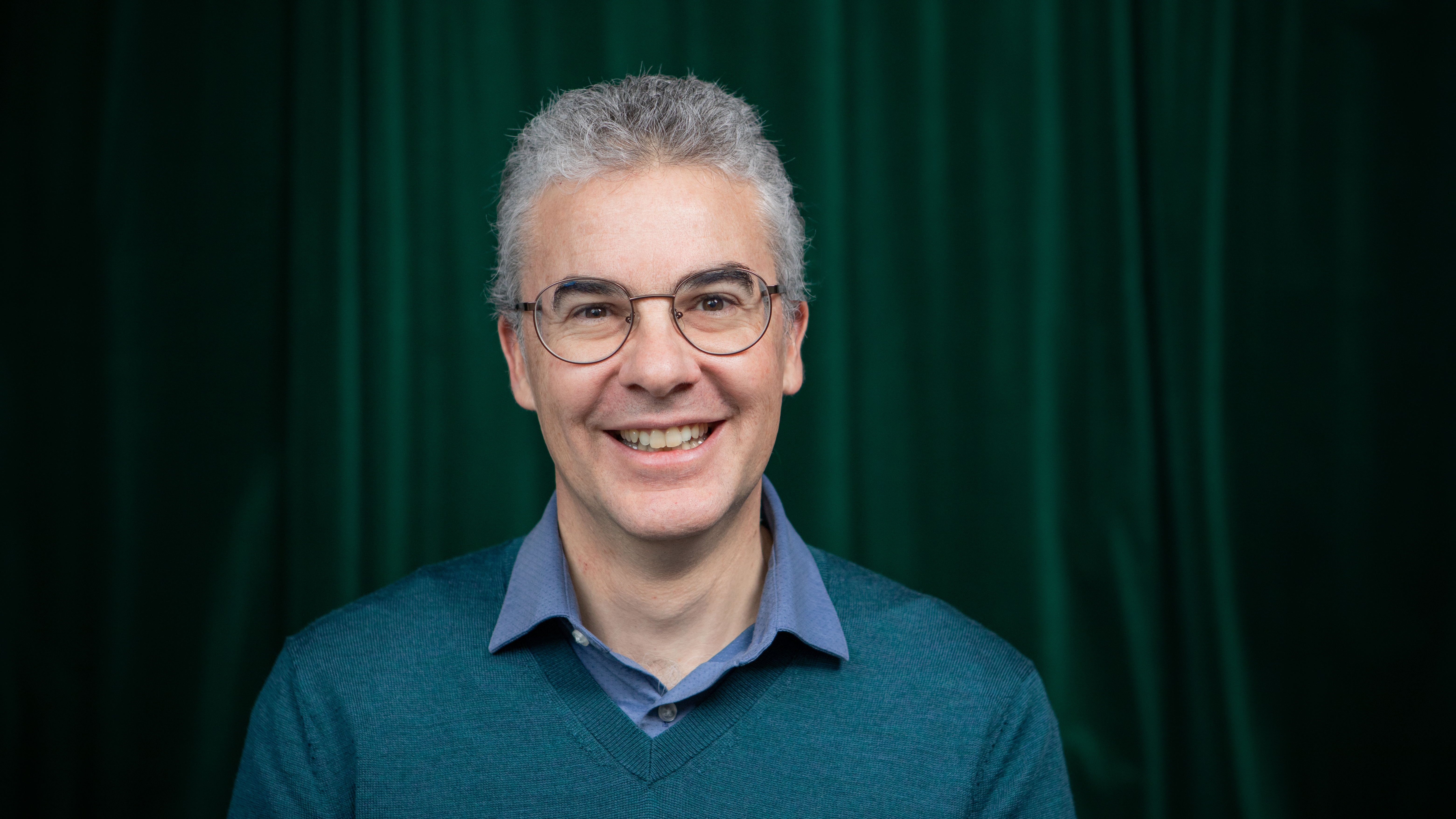 En leende man med glasögon, grått hår och blå tröja.