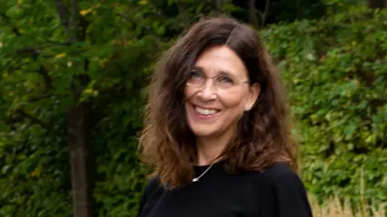 A person with dark curly hair and glasses.