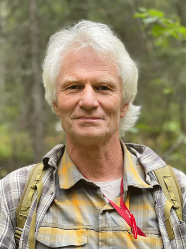 En person med vitt hår står i skogen.