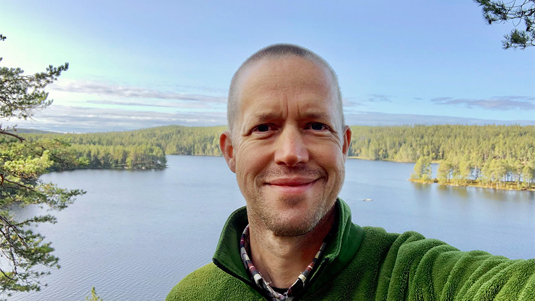 En person i grön fleecetröja stående på en höjd med ett vattendrag i bakgrunden