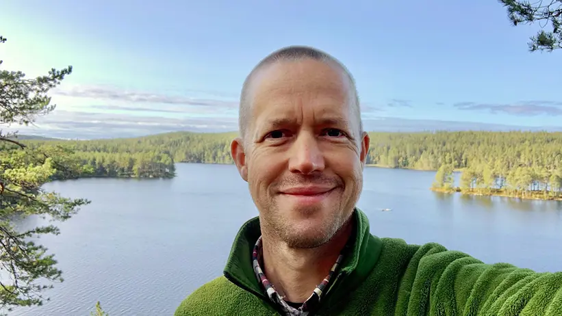 En person i grön fleecetröja stående på en höjd med ett vattendrag i bakgrunden