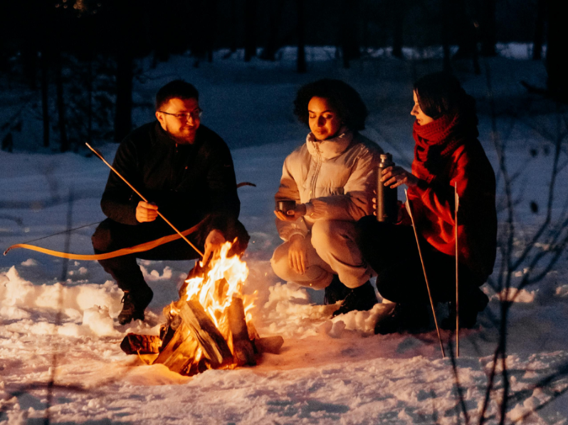 Tre personer sitter vid en eld