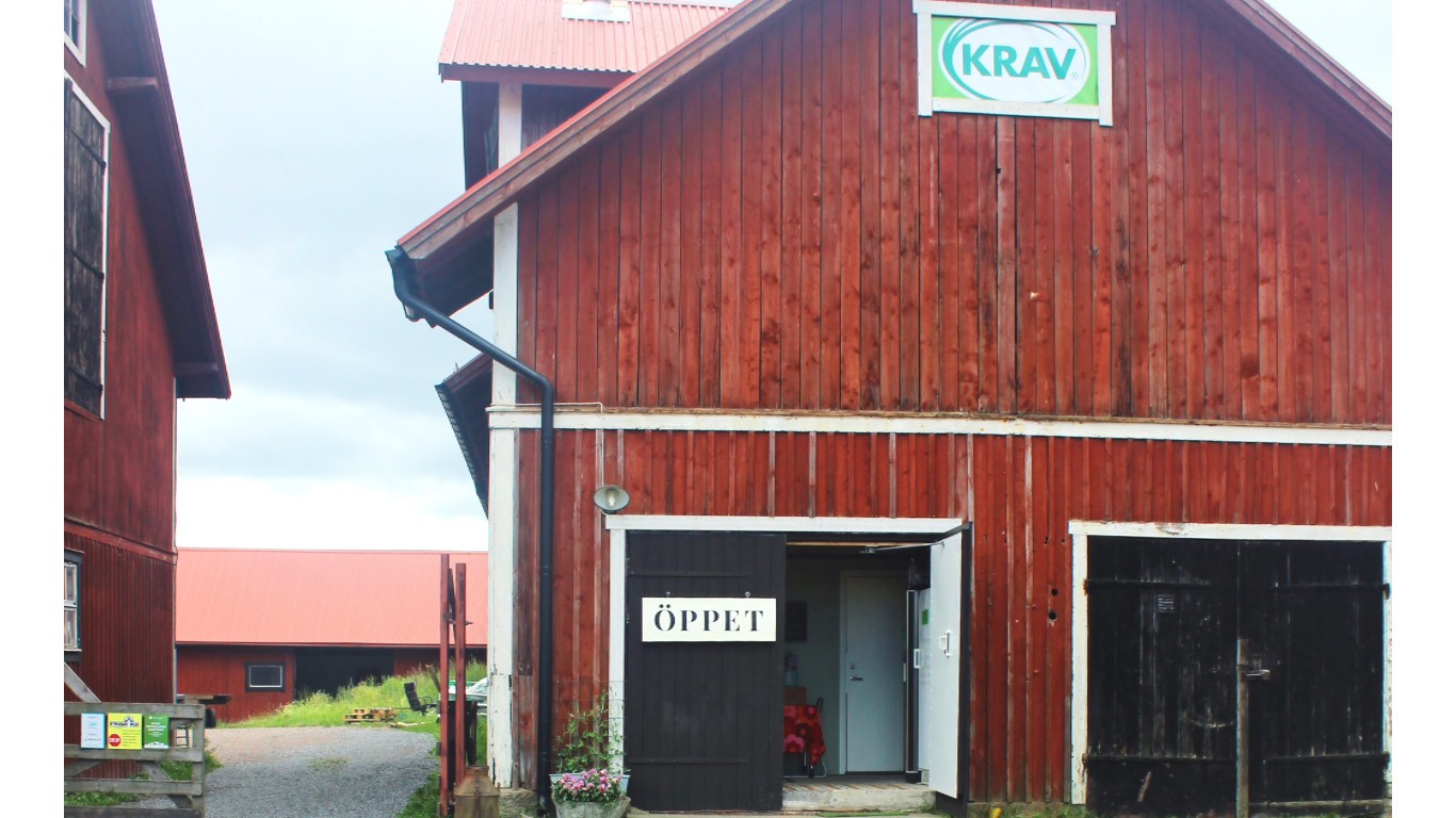 En röd lada med gårdsbutik. En skylt "öppet" och en skylt "KRAV" syns på fasaden. Foto.
