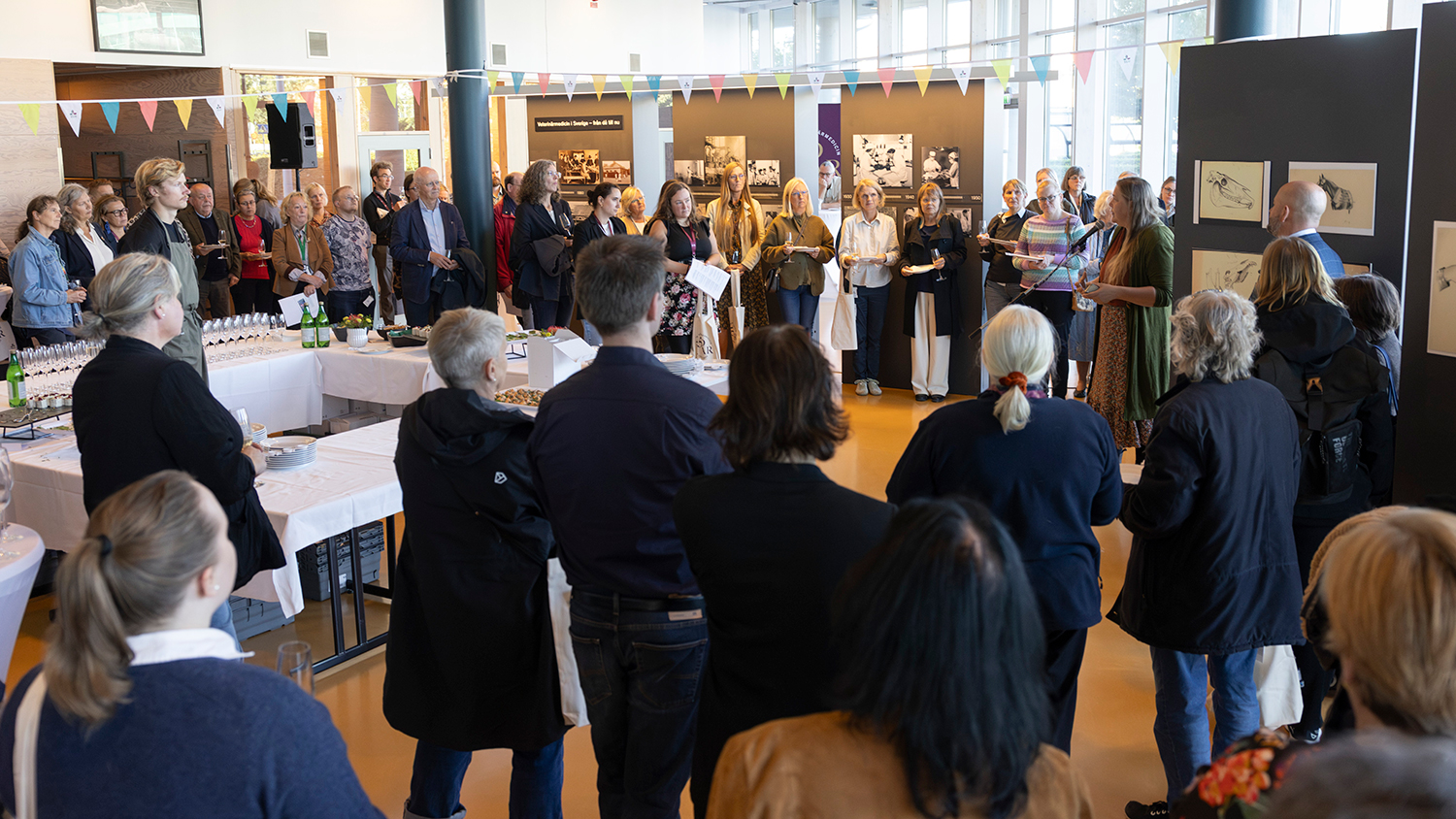 Många människor står i utställningen, runt ett bord med snittar och bubbel, och lyssnar på Marte Rodal som berättar om Hilma af Klint
