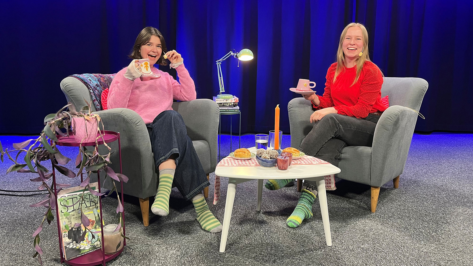 Två unga kvinnor sitter i en studio i var sin fåtölj och pratar och dricker kaffe.