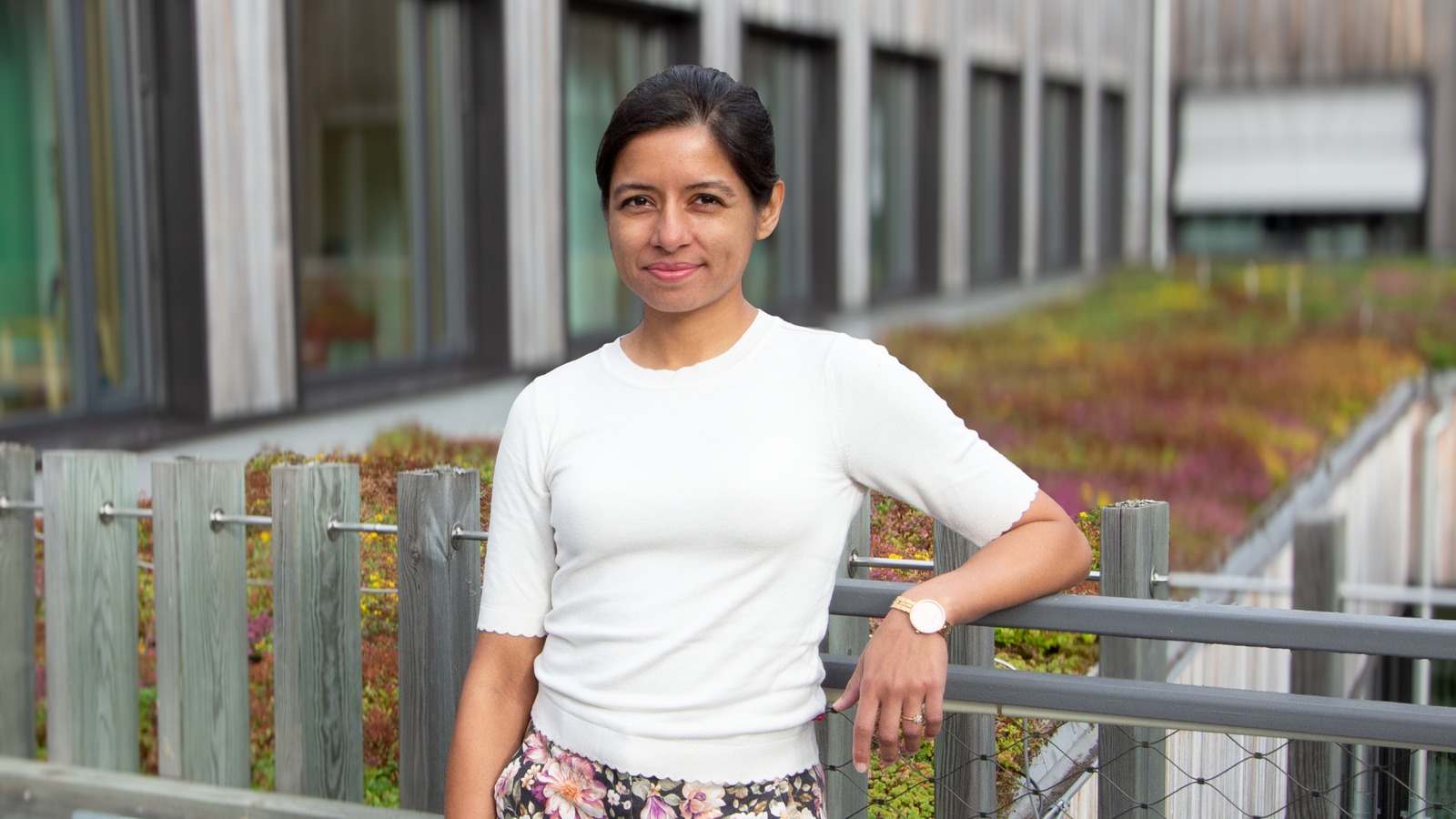 Mallika Sardeshpande står vid ett räcke med ett växtklätt tak i bakgrunden.