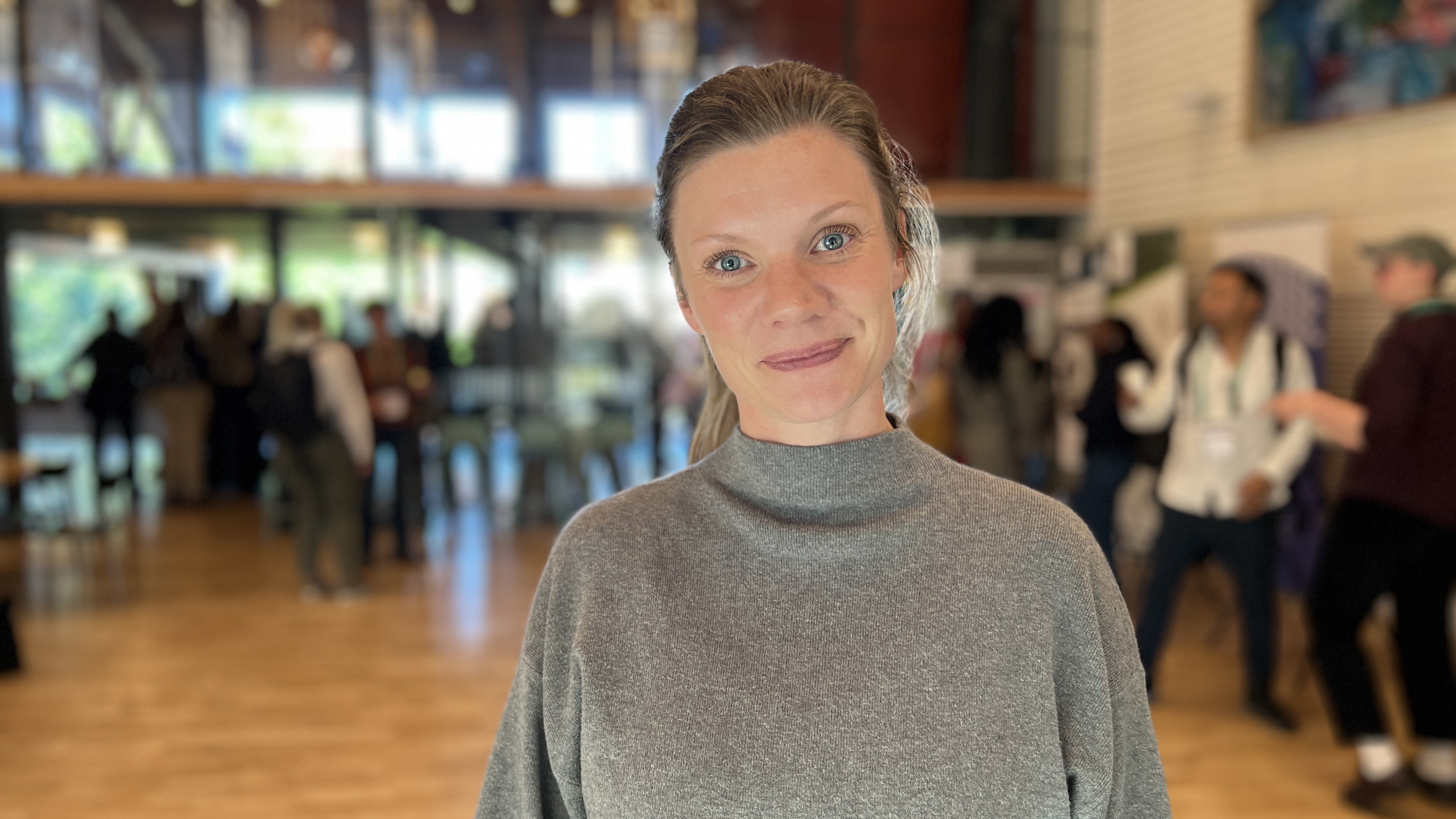 A woman in a conference environment, with people, life and movement in the background. Photo.