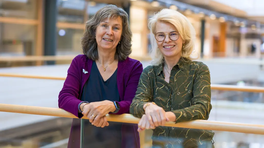 Två leende kvinnor vid ett räcke. Foto.