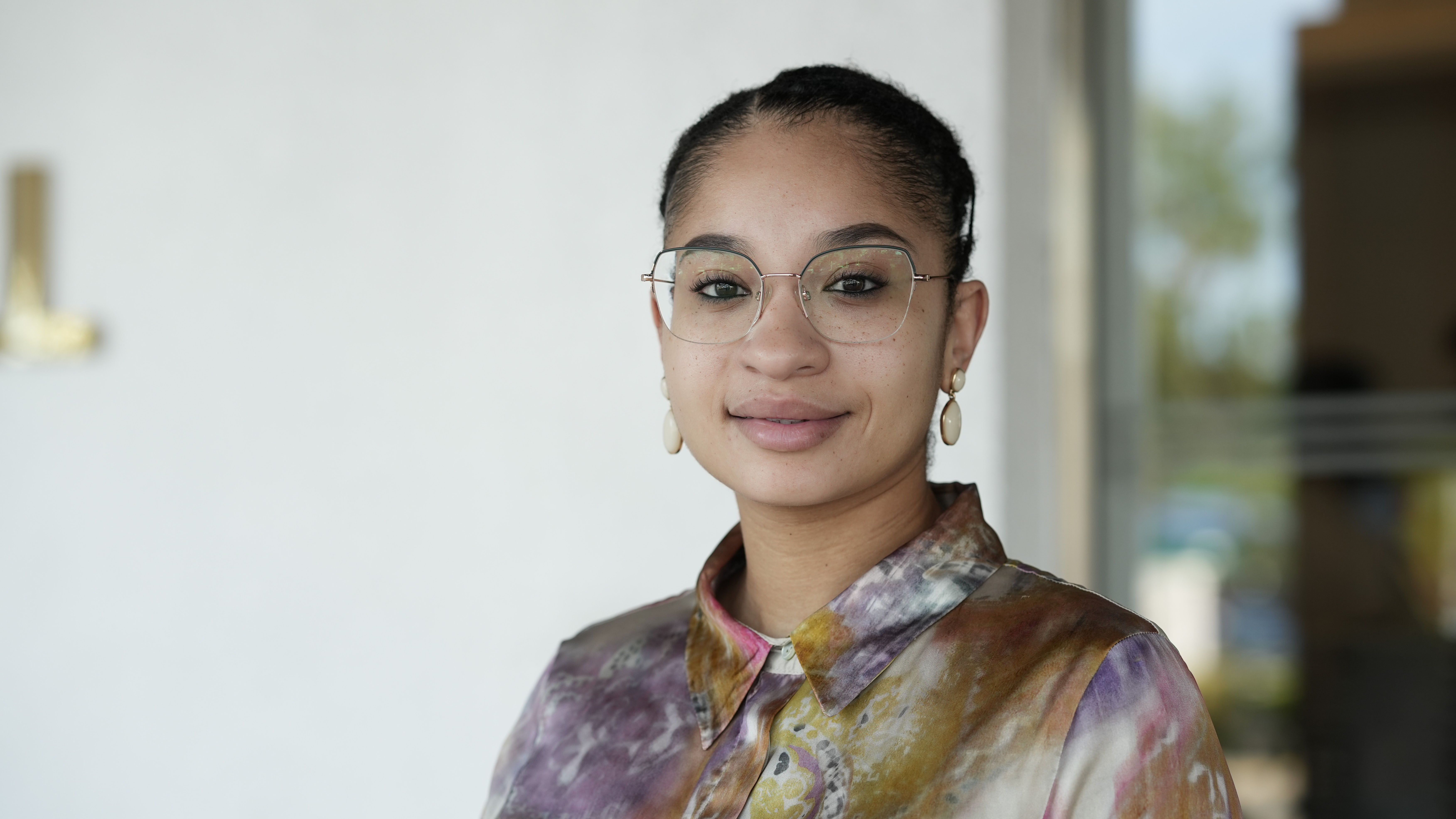 En kvinna med glasögon, örhängen och en spräcklig blus. Foto.