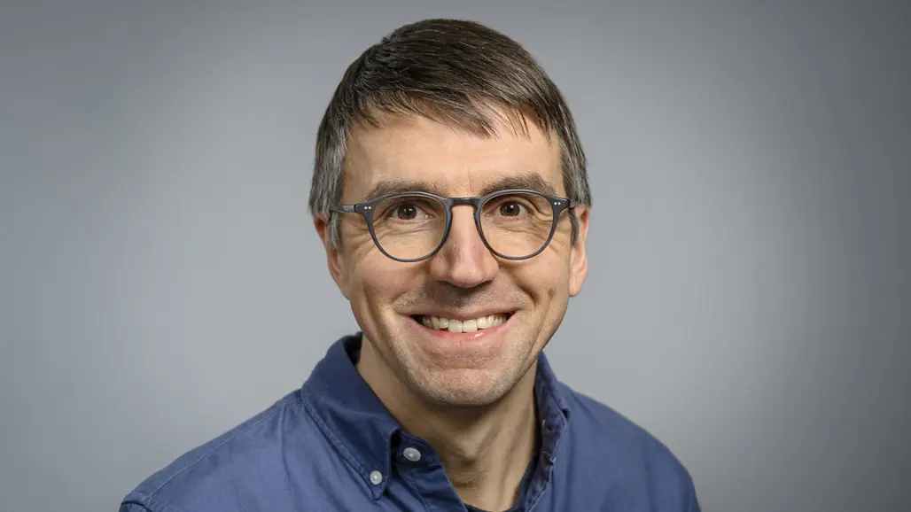 Portrait photo of Thomas Wieloch in front of a blue-grey background