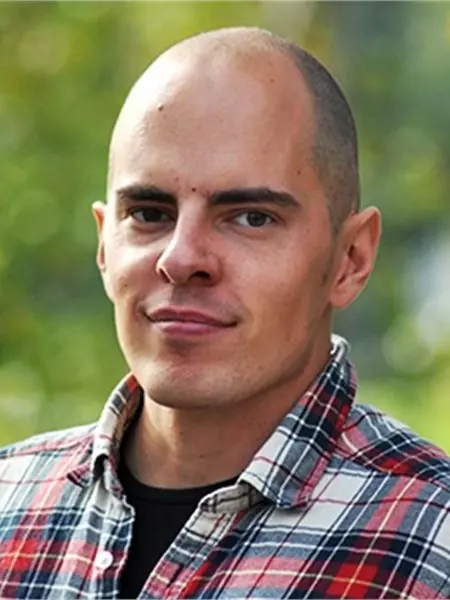 Porträtt av Marcus Larsson, han har rakat hår och bär en rutig skjorta