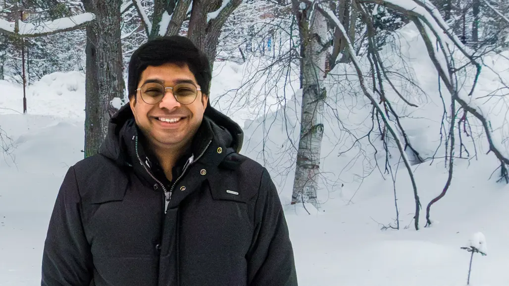 Porträttfoto av Vinod Kumar stående med en svart jacka i ett snöigt landskap framför några träd i bakgrunden
