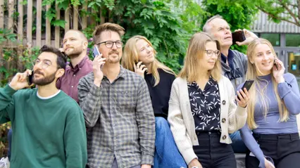 7 personer som är utomhus. Alla håller i en varsin mobil och verkar vara i ett telefonsamtal.