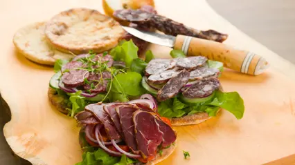 Delikatesser av renkött på en bricka med sallad och en fin kniv. Foto Shutterstock.