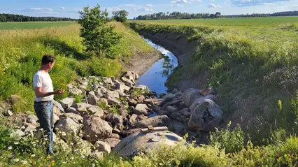 A person standing by a ditch between two fields.
