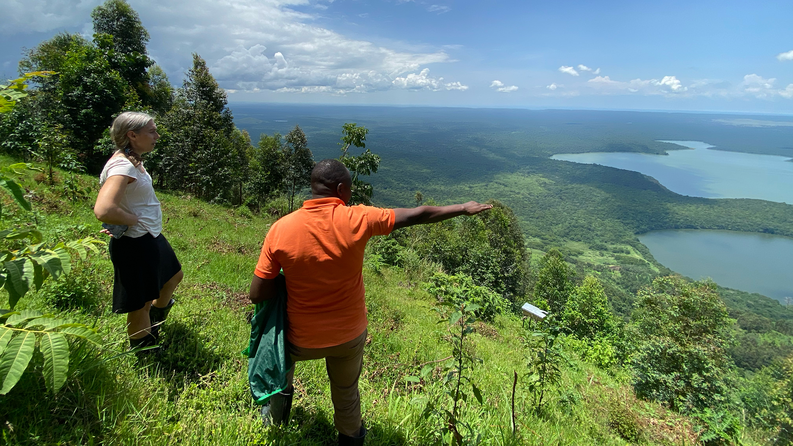 Two persons standing in a slope, surrounded by lush green vegetation, looking out over a hollow. One of the persons point something out. 