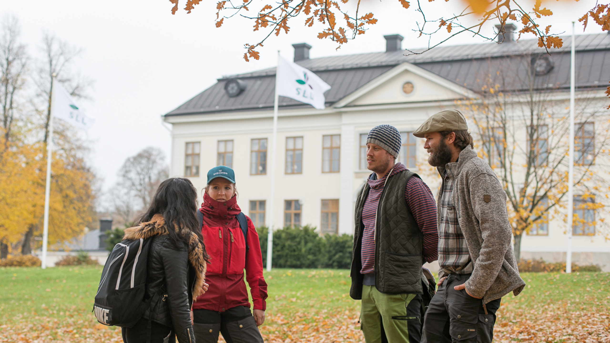 Fyra unga personer och en hund står framför en stor gammal herrgårdsbyggnad.