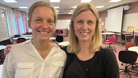 Två blonda kvinnor står tätt intill varandra och ler in mot kameran