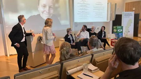 Fem personer på scen i plenisal