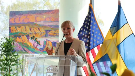 Woman speaks standing with flags behind