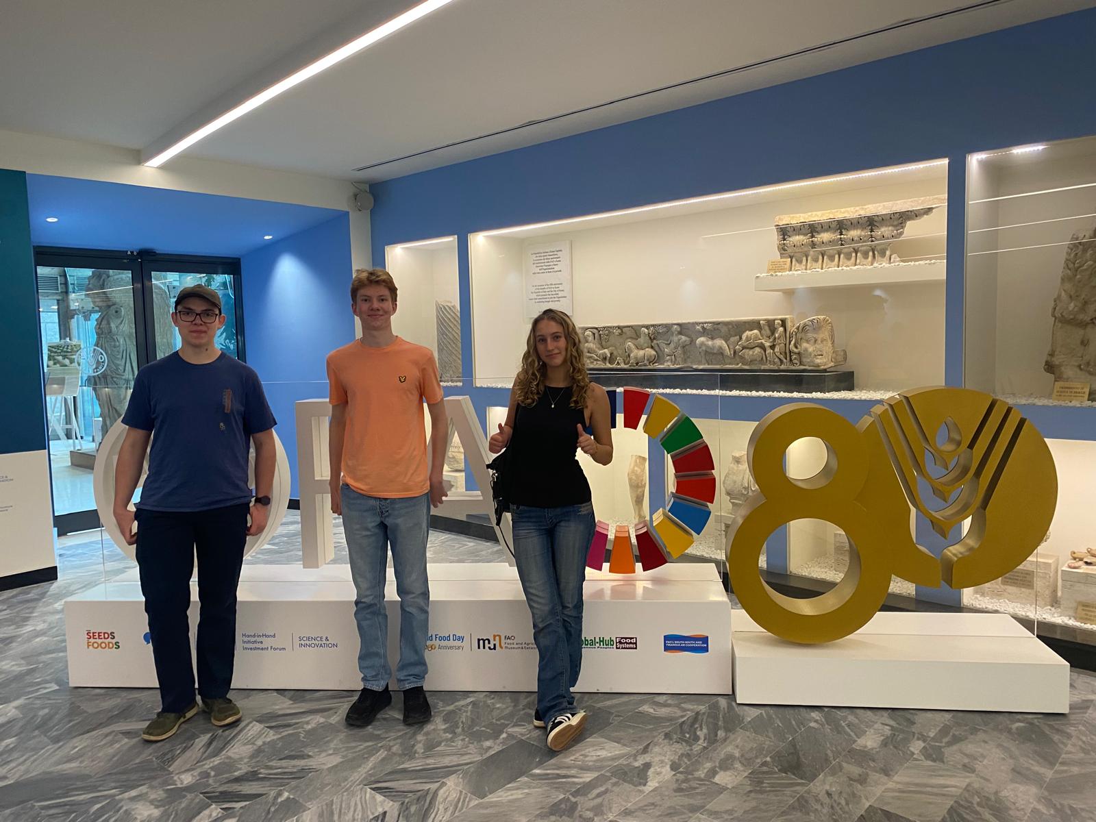 Three persons in front of the FAO sign