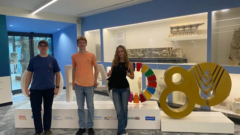 Three persons in front of the FAO sign