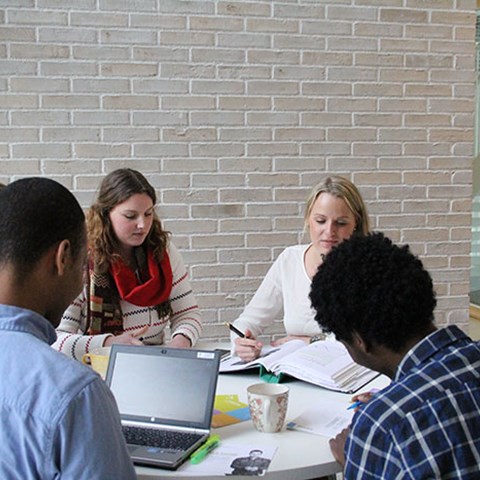 Students engaged in group work with computer, binder, notebooks and coffee cup on table. Photo.