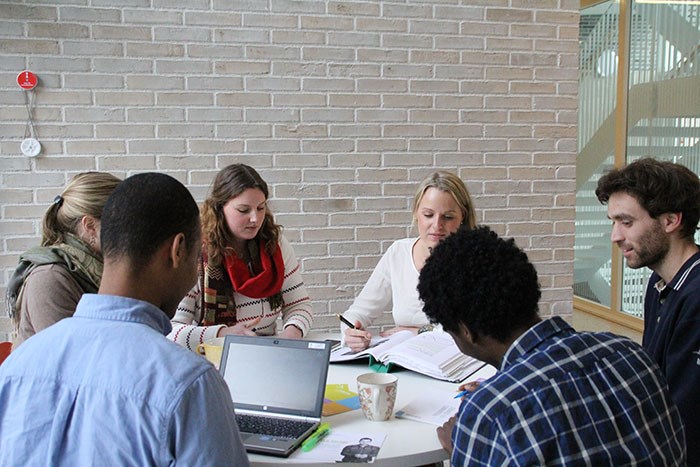 Studenter engagerade i grupparbete med dator, pärm, anteckningsblock och kaffekopp på bordet. Foto.