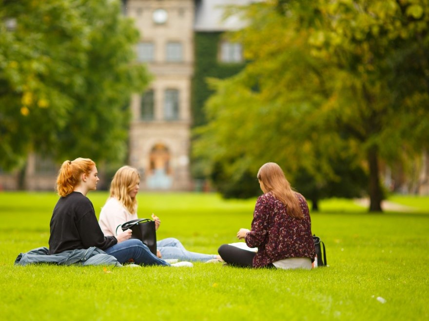 Tre kvinnliga studenter sitter på gräsmattan i Alnarsparken, foto.